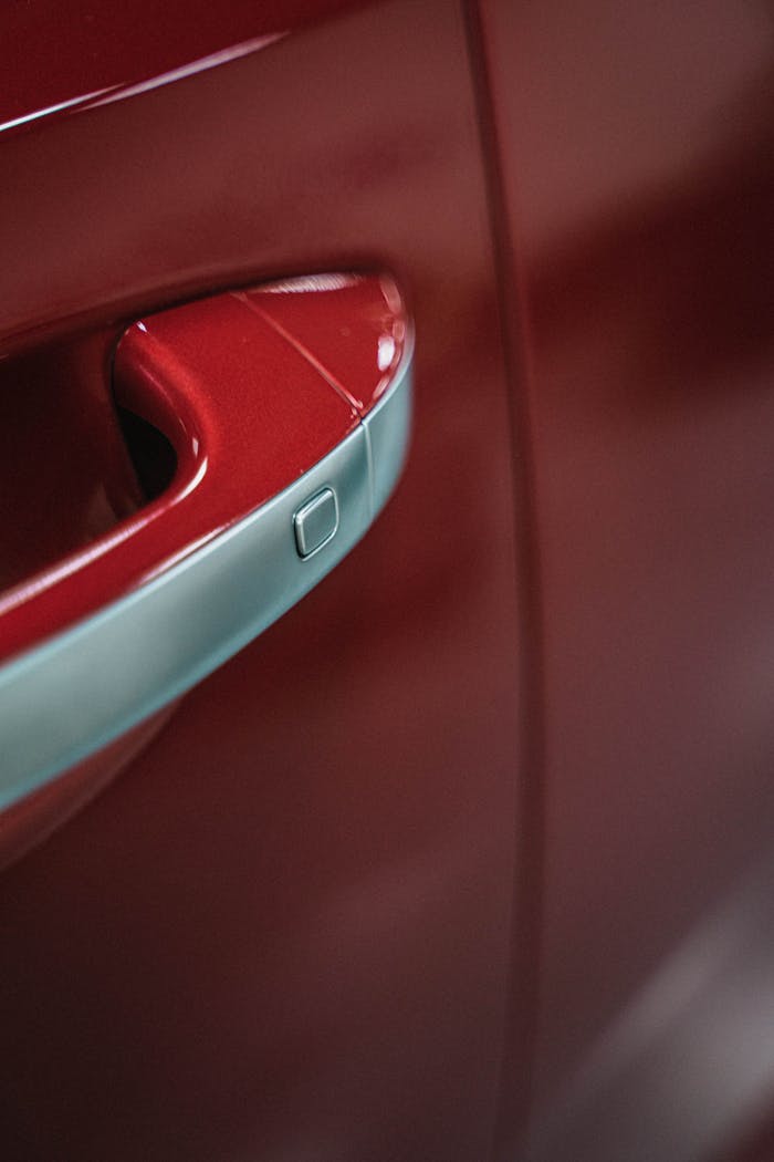 Close-up view of a shiny red car door handle reflecting light and details.